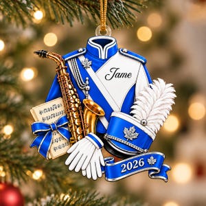 May include: A blue and white marching band uniform ornament featuring a gold saxophone, white gloves, a sheet music book with a blue bow, and a shako hat with a white plume. The uniform is personalized with the name Jame and the year 2026.