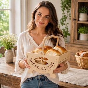 May include: A light-colored wooden bread basket with a curved handle and feet, featuring a cutout design of a wheat stalk and the text BREAD BASKET on the side, containing several round, golden-brown baked bread rolls.