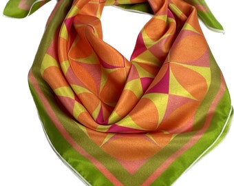 May include: A colorful silk scarf with a geometric pattern. The scarf features a vibrant design with orange, yellow, and pink shapes, framed by a green border. The scarf is folded, showcasing its texture and design.