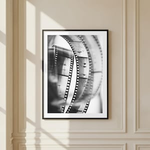 Könnte beinhalten: Ein schwarz-weiß gerahmter Wandkunstdruck mit einer Nahaufnahme von aufgerollten 35-mm-Fotofilmstreifen. Der Film zeigt kleine, sich wiederholende Silhouetten von Figuren vor einem hellen Hintergrund, gefasst in einem schlichten schwarzen Rahmen.