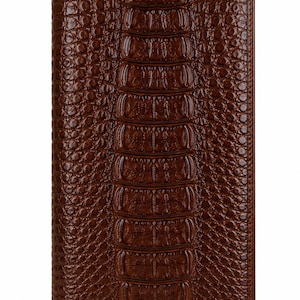 Pode incluir: Uma carteira retangular castanha com acabamento brilhante e uma textura em relevo que imita a aparência de pele de crocodilo, com um painel central vertical de escamas retangulares maiores ladeado por escamas mais pequenas e arredondadas.