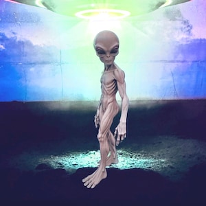 Puede incluir: Una figura extraterrestre gris y esbelta con cabeza alargada, ojos grandes y oscuros y musculatura definida. La figura se muestra de perfil, iluminada por una fuente de luz verde circular y brillante situada directamente sobre su cabeza.