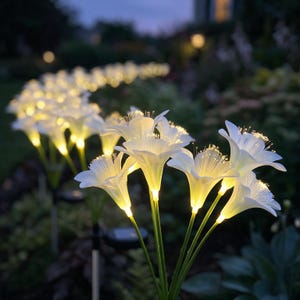 May include: A series of solar-powered garden lights shaped like white lily flowers. Each flower features a glowing center with thin, illuminated filaments extending outward, mounted on thin green stems that are arranged in a curved path.