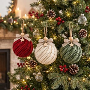 Può includere: Tre decorazioni natalizie rotonde appese a un albero, caratterizzate da una trama all'uncinetto nei colori rosso, crema e verde. Ogni decorazione è sormontata da un fiocco in tessuto beige, una piccola stella in legno e un cordino in iuta.