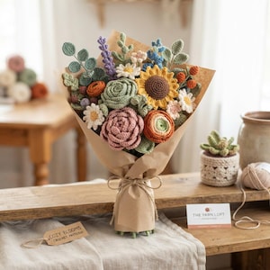 May include: A bouquet of crocheted flowers wrapped in brown paper, featuring a yellow sunflower, pink and green roses, white daisies, lavender, and orange buds. A tag labeled COZY BLOOMS CROCHET PATTERN and a card for THE YARN LOFT are visible.