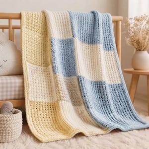 Könnte beinhalten: Eine grob gestrickte Decke mit einem Karomuster aus hellgelben, cremefarbenen und hellblauen Quadraten. Die Decke weist durchgehend ein strukturiertes Waffelmuster auf, das ihr ein dickes und weiches Aussehen verleiht, während sie über einem Holzbett hängt.