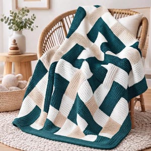Peut inclure: Un plaid tricoté présentant un motif géométrique de blocs rectangulaires alternés bleu sarcelle, blancs et beiges. La couverture est drapée sur une chaise en bois incurvée, mettant en valeur une texture en maille épaisse aux bords nets.