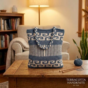 May include: A blue and white knitted tote bag featuring a repeating wave pattern on the top and bottom sections, a vertical striped center panel, and braided handles. The text TERRACOTTA HANDKNITS Est. 2024 is printed in the bottom right corner.