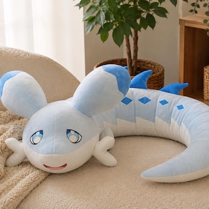 May include: A long, soft plush toy shaped like a creature with a light blue and white body. It features large, rounded ears, blue diamond-shaped markings along its back, small blue dorsal fins, and a face with large blue eyes and a small red mouth.