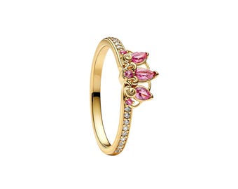 May include: A gold ring featuring a band encrusted with small clear stones. The top of the ring displays a crown-like design with three pear-shaped pink gemstones and intricate gold scrollwork accents set against a polished gold finish.