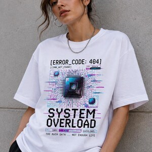 Può includere: Una t-shirt bianca a maniche corte con una stampa grafica che riporta il testo ERROR_CODE: 404, CONN_NOT_FOUND, CRY AGAIN, SYSTEM OVERLOAD, CPU: 100% e TOO MUCH DATA ... NOT ENOUGH LIFE, insieme a un'illustrazione di un chip per computer.