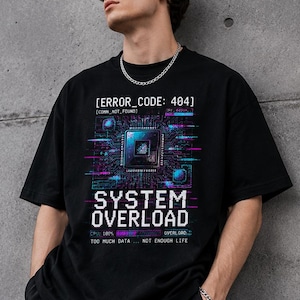Può includere: Una t-shirt nera a maniche corte con una stampa grafica che riporta il testo ERROR_CODE: 404, SYSTEM OVERLOAD, CPU: 100% e TOO MUCH DATA... NOT ENOUGH LIFE. Il design include un'illustrazione di un chip di elaborazione centrale con linee di circuito blu e viola.