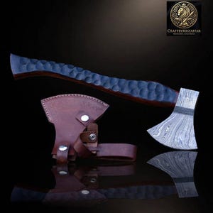 May include: A hand axe with a patterned Damascus steel blade and a dark, textured wooden handle featuring a dimpled surface. A brown leather sheath with silver-colored metal snap buttons is positioned next to the axe head.