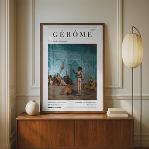 May include: A framed art print titled Gérôme The Snake Charmer 1879, featuring a reproduction of the oil painting depicting a figure with a snake in a blue-tiled room. The print includes text detailing the artist, medium, and location.
