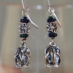 May include: Silver dangle earrings with a silver flower charm and blue and green iridescent beads. The earrings feature a silver charm of a pair of flip flops.