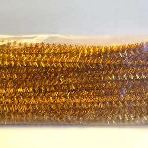 May include: A package of gold metallic pipe cleaners. The pipe cleaners are tightly packed together, creating a dense, textured appearance. The gold color is bright and reflective, suggesting a festive or decorative use. The package is sealed in clear plastic.