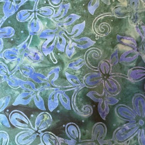 May include: A green and blue fabric with a floral pattern. The flowers are blue and white and have a batik style.