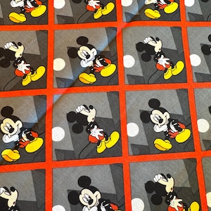 May include: A fabric featuring a repeating pattern of Mickey Mouse. Each Mickey Mouse is in a different pose, set against a gray background with a white circle and black geometric shapes. The pattern is framed by a red grid.