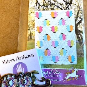 May include: A quilt pattern for a quilt titled "Love Bugs". The quilt features a white background with a repeating pattern of colorful hearts. The pattern is by "Singing Doe Quilts Designs".