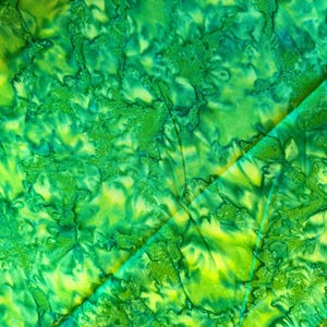 May include: Close-up of a fabric with a vibrant, abstract pattern. The design features a blend of green and yellow hues, creating a textured, organic appearance. The fabric is folded, revealing the pattern's depth and complexity. The overall effect is visually striking.