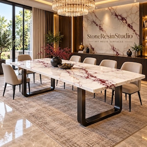 May include: A rectangular dining table with a white surface featuring prominent red marble veining, supported by two thick, black U-shaped metal legs. The table is surrounded by six beige upholstered chairs with dark legs in a room setting.