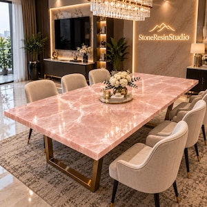 Puede incluir: Una mesa de comedor rectangular con una superficie de piedra rosa pulida con vetas blancas, sostenida por un marco de metal dorado. La mesa está rodeada por seis sillas beige tapizadas con patas oscuras, creando un conjunto de muebles coherente.