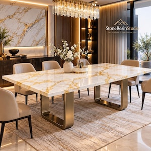 Op de afbeelding: Een rechthoekige eettafel met een wit en goudkleurig marmeren blad en twee U-vormige poten van geborsteld goudkleurig metaal. De tafel is omringd door zes beige gestoffeerde stoelen. Een witte vaas met witte bloemen staat op het tafelblad.