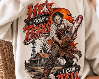 May include: A beige crewneck sweatshirt featuring a graphic print of a masked figure holding a blood-stained chainsaw. The text reads HE'S FROM TEXAS and I CAN TELL. The background includes a farmhouse, a windmill, and a large orange moon.