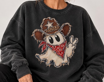 Può includere: Una felpa girocollo grigio antracite con una stampa centrale raffigurante un fantasma bianco che indossa un cappello da cowboy marrone con fascia leopardata e una bandana rossa paisley, mentre fa il segno di vittoria.