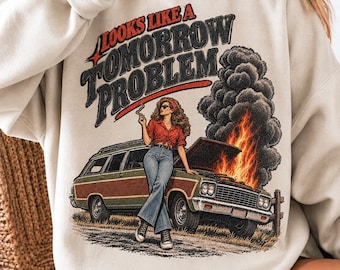 May include: A cream-colored crewneck sweatshirt featuring a graphic print of a person leaning against a station wagon with a smoking, burning engine. The text reads "LOOKS LIKE A TOMORROW PROBLEM" in a distressed, bold, dark-colored font.