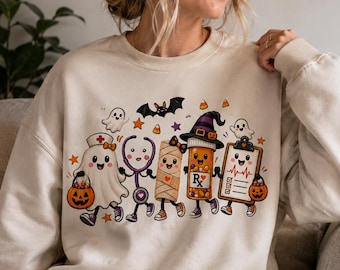Può includere: Una felpa girocollo color beige con una grafica colorata di personaggi medici in stile cartone animato che festeggiano Halloween, tra cui un fantasma infermiere, uno stetoscopio, una mummia, un flacone di pillole e una cartella clinica.