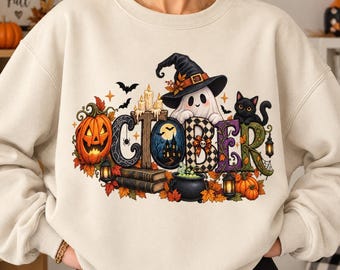 Può includere: Una felpa girocollo color crema con una stampa grafica che forma la parola OCTOBER. Il design include una zucca, un fantasma con un cappello da strega, un gatto nero, candele, libri, un calderone e pipistrelli, decorati con foglie autunnali.