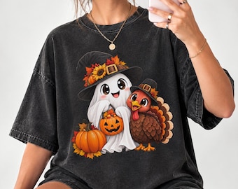 Può includere: Una t-shirt grigio antracite a maniche corte con una stampa grafica di un fantasma bianco con cappello da strega e un tacchino marrone con cappello da pellegrino. Il fantasma tiene in mano una piccola zucca e accanto c'è una zucca grande.