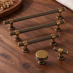 May include: A collection of antique brass cabinet hardware featuring a textured, woven-style pattern. The set includes three long bar pulls of varying lengths, one round knob, and one T-shaped knob, all displaying the text VelaideDesign.