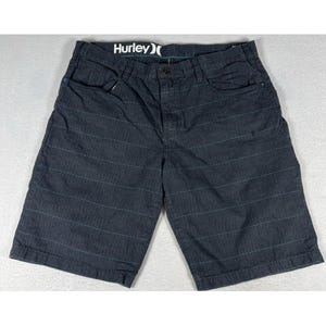 May include: Dark charcoal gray shorts featuring a subtle horizontal pinstripe pattern in a lighter blue tone. The shorts include a button and zipper fly closure, belt loops, and a black interior waistband label with the white text Hurley.