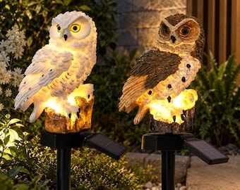 May include: Two solar-powered garden lights shaped like owls perched on tree stumps. One owl is white with yellow eyes, and the other is brown and white with dark eyes. Both figures are illuminated from below and mounted on black stakes.