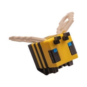 May include: A blocky, cubic bee figurine featuring a yellow body with horizontal black stripes, small black antennae, and light blue square eyes. The figure has off-white, pixelated wings extending from its back, designed with a distinct grid pattern.