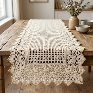 May include: A cream-colored crochet table runner featuring a central rectangular grid pattern and an intricate scalloped border with metallic gold thread accents. The runner is elongated with a pointed edge design along the entire perimeter.