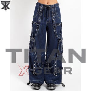 May include: Dark blue denim cargo pants featuring multiple adjustable straps, silver-toned metal grommets, D-rings, and studded accents. The wide-leg trousers include a drawstring waist and large side pockets, with the text TITAN X GEAR overlaid.