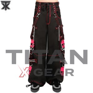 May include: Black cargo pants featuring red contrast stitching, silver chains, and metal D-rings. The legs display bright pink skull graphics and studded straps. The waistband includes a drawstring and belt loops. The text TITAN X GEAR is visible.