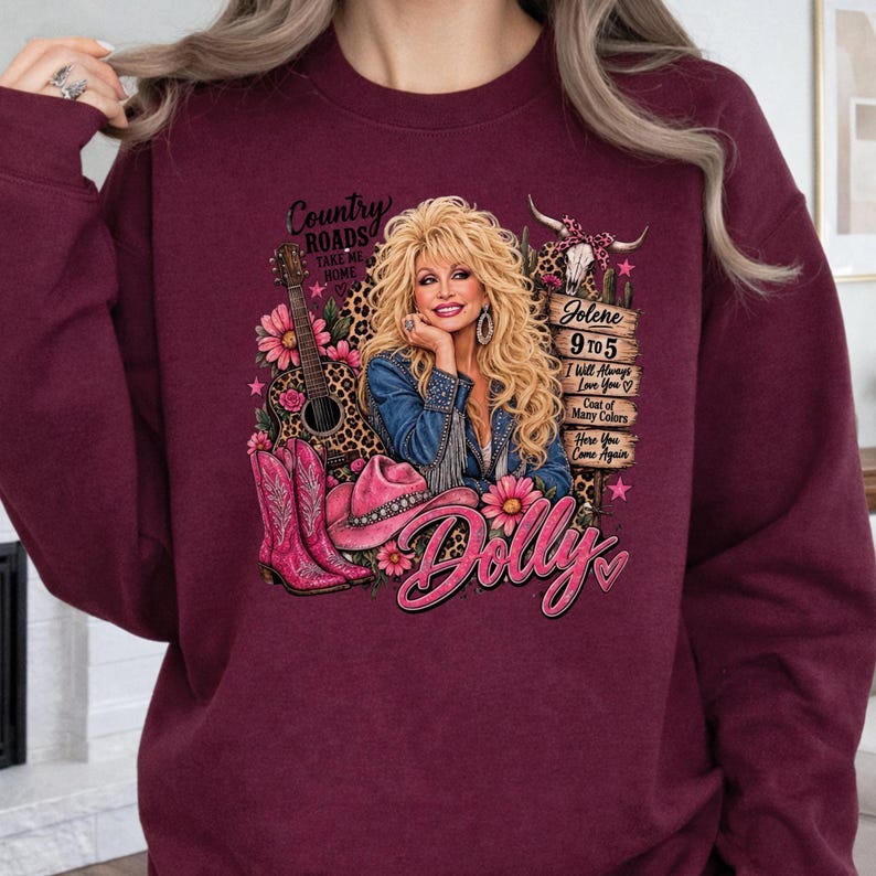 May include: A maroon crewneck sweatshirt featuring a graphic print of Dolly Parton with blonde hair, a guitar, pink cowboy boots, a pink hat, and a cow skull. The text includes Country Roads, Jolene, 9 to 5, I Will Always Love You, and Dolly.