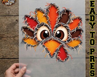 May include: A DTF transfer sheet featuring a cartoon turkey graphic with frayed denim-style edges. The turkey has large brown eyes, a bright orange beak, and a fan of feathers in shades of red, orange, and brown. The design is on a clear film.