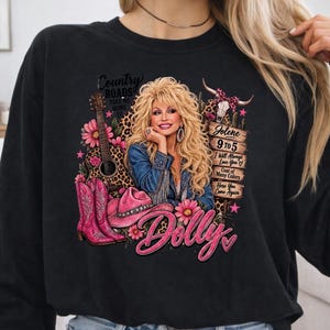 May include: A black long-sleeve sweatshirt featuring a graphic print of Dolly Parton with blonde hair, a denim jacket, a guitar, pink cowboy boots, a pink hat, and a wooden sign listing song titles like Jolene, 9 to 5, and I Will Always Love You.