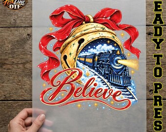 May include: A DTF transfer sheet featuring a graphic of a large gold bell adorned with a red ribbon. Inside the bell is a steam train traveling through a snowy landscape. The word Believe is written in red script below the train and bell.