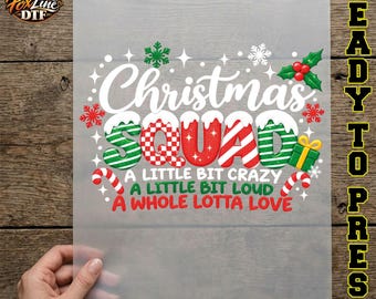 May include: A transparent DTF transfer sheet featuring the text Christmas SQUAD in white, red, and green patterns with snow accents. Below, the text reads A LITTLE BIT CRAZY, A LITTLE BIT LOUD, A WHOLE LOTTA LOVE, decorated with snowflakes, holly, and candy canes.