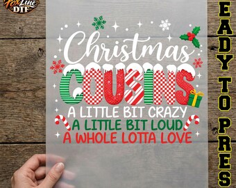 May include: A clear DTF transfer sheet featuring the text Christmas COUSINS in white and red-green patterns, with the phrases A LITTLE BIT CRAZY, A LITTLE BIT LOUD, and A WHOLE LOTTA LOVE in green and red, accented by snowflakes and candy canes.