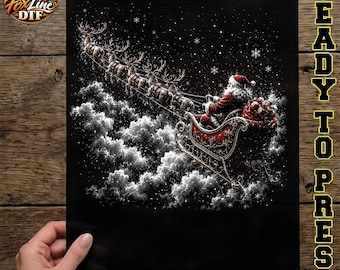 May include: A black DTF transfer sheet featuring a graphic of Santa Claus in a red suit riding a sleigh pulled by a team of reindeer through a starry night sky above white clouds. The text FoxLine DTF and READY TO PRESS are visible.