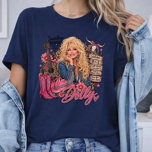 May include: A navy blue t-shirt featuring a graphic print of a blonde woman with a guitar, pink cowboy boots, a pink hat, and a wooden sign listing song titles including Jolene, 9 to 5, I Will Always Love You, and Coat of Many Colors.
