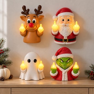 Könnte beinhalten: Vier dekorative Figuren, bestehend aus einem braunen Rentier, einem Weihnachtsmann, einem weißen Geist und einer grünen Kreatur im roten Anzug. Jede Figur hat zwei kleine, beleuchtete gelbe Hände, die beidseitig den Mittelfinger zeigen.