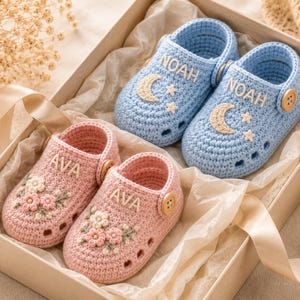 Pode incluir: Dois pares de sapatinhos de bebé feitos à mão em croché numa caixa de presente. Um par é azul claro com o nome NOAH e um design de lua e estrela. O outro par é rosa claro com o nome AVA e um bordado floral. Cada sapato tem um botão de madeira.